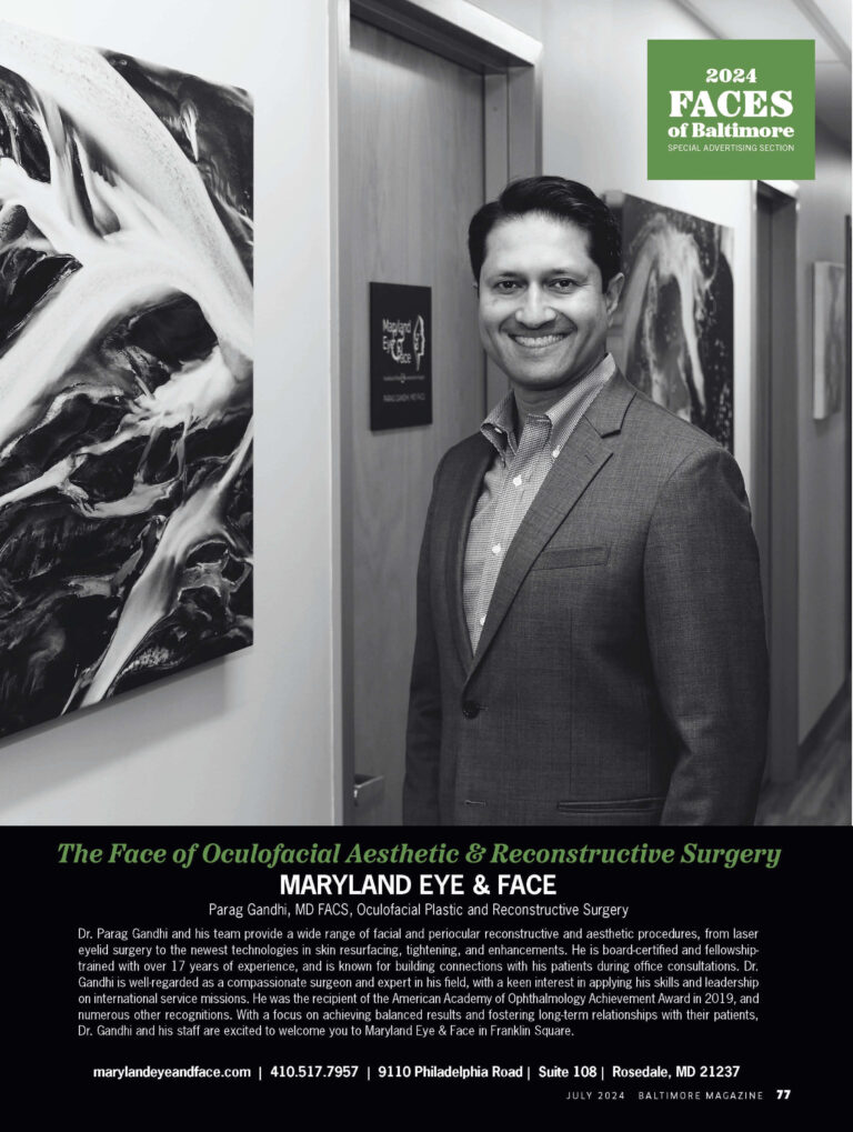 Dr. Parag Gandhi in a suit stands in a hallway adorned with abstract art. Overhead text reads "2024 Faces of Baltimore," signifying professional recognition.