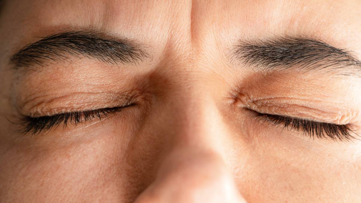 Close-up of a person's face with eyes tightly shut, showcasing furrowed brows. The expression suggests tension or concentration.