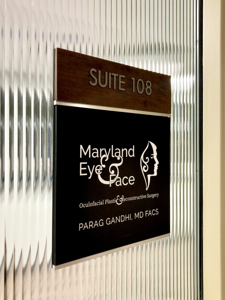 Sign for "Suite 108" with a black plaque stating "Maryland Eye & Face" and detailing oculofacial plastic surgery. Elegant and professional design.